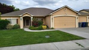 A single-story house with a garage, a front door, and a small front yard with a lawn and a flower bed. - Tri-Cities Home Away From Home (Richland)