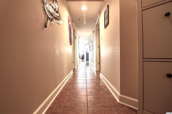 A hallway with a tiled floor, beige walls, and a door at the end. - Pristine Condo at Beachwalk Villas in North Myrtle Beach, SC Cherry Grove. (North Myrtle Beach)