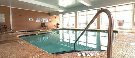 An indoor swimming pool with clear signage, a tiled floor, and a view of the outside through large windows.