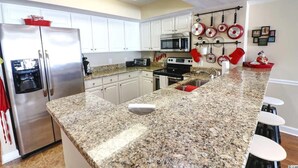A kitchen with white cabinets, a granite countertop, stainless steel appliances, and red cookware hanging on the wall. - Pristine Condo at Beachwalk Villas in North Myrtle Beach, SC Cherry Grove.  (North Myrtle Beach)
