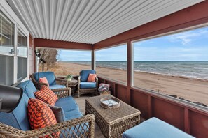 A covered outdoor seating area with wicker furniture, a view of the beach, and a large window.