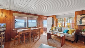 A wooden cabin interior with a dining area, sofa, and large windows overlooking the ocean. - Private Beach, Outdoor Dining, Firepit (Oostburg)