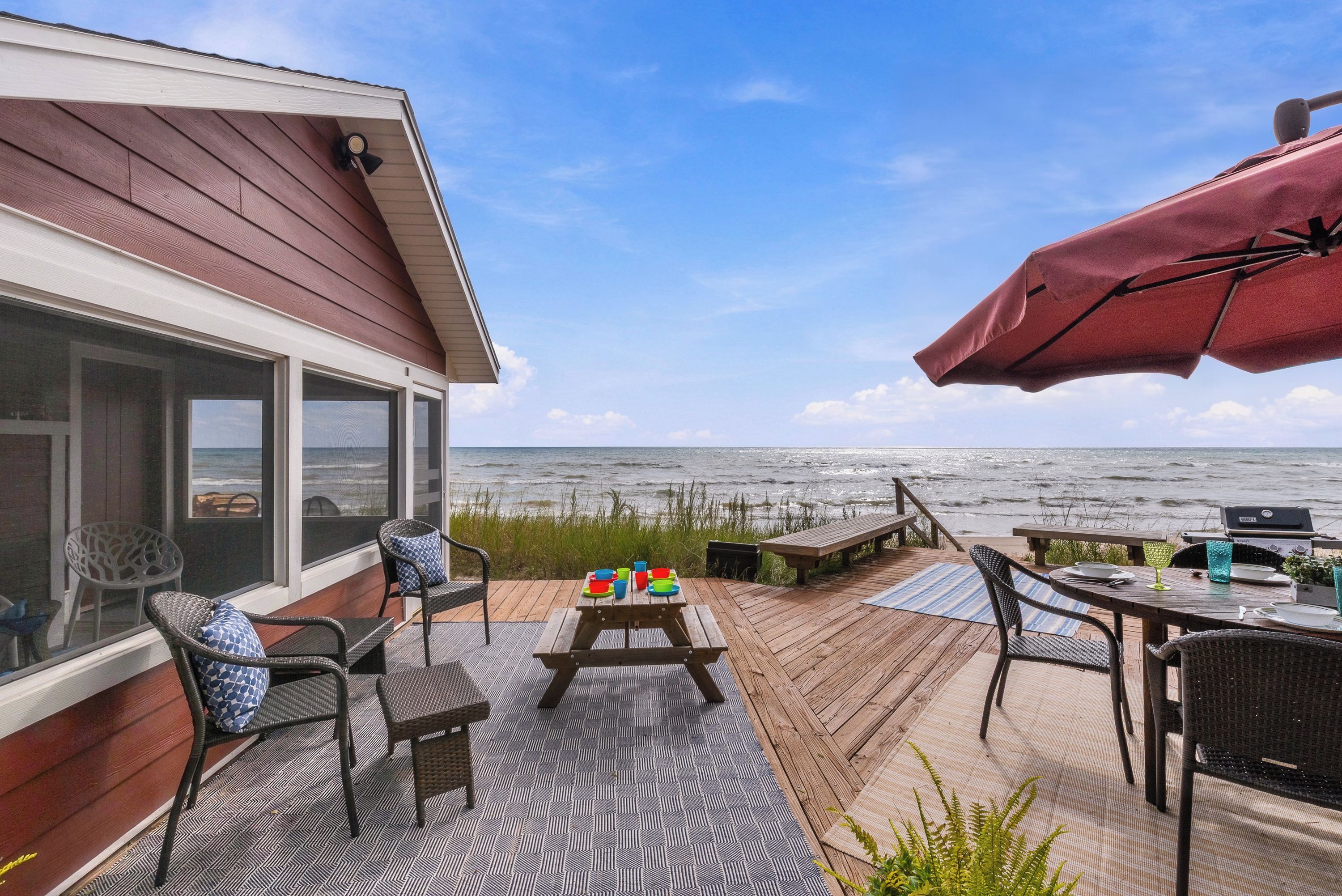 A deck with outdoor furniture, a grill, and a view of the ocean.