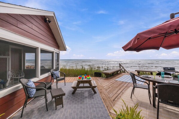 A deck with outdoor furniture, a grill, and a view of the ocean.
