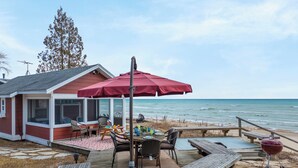 A wooden deck with a table and chairs, a red umbrella, and a barbecue grill. - Private Beach, Outdoor Dining, Firepit (Oostburg)