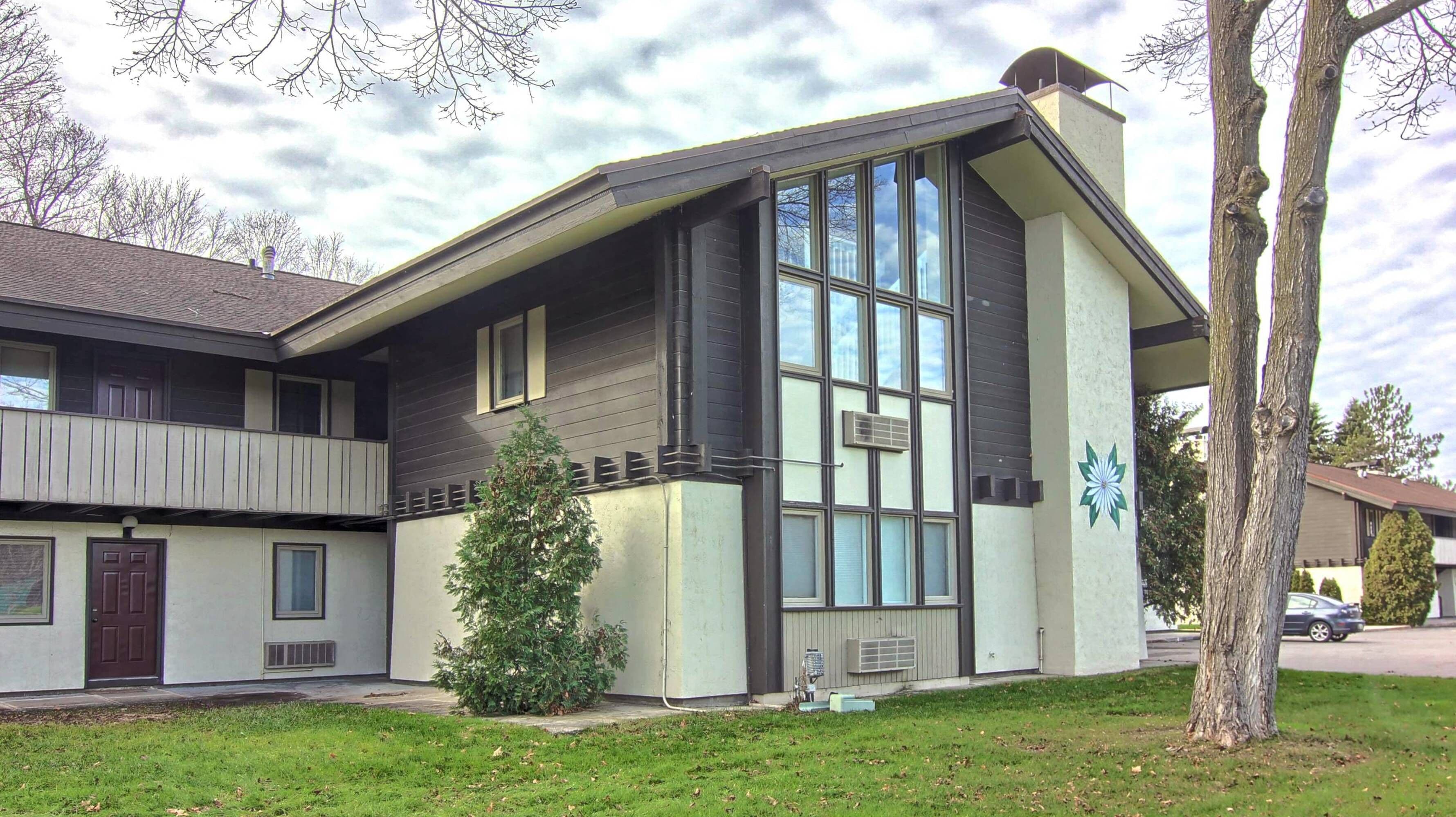 A two-story building with a flat roof, large windows, and a small tree in the front yard.