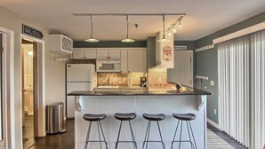 A modern kitchen with a central island, bar stools, a microwave, and a refrigerator.