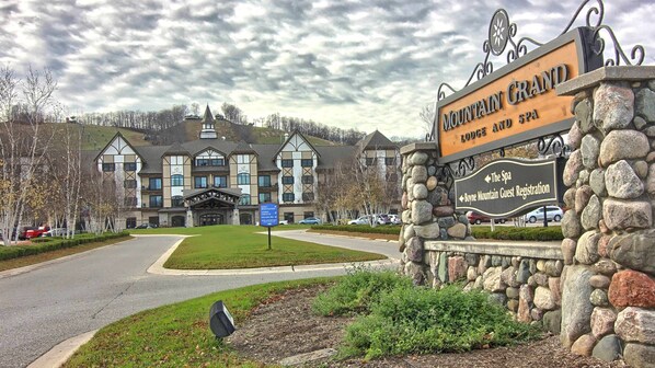 A large, multi-story building with a prominent entrance and a stone sign indicating 'Mountain Grand Lodge and Spa'.