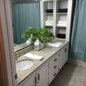 Une salle de bain avec deux lavabos, un miroir, un rideau de douche et une étagère avec des serviettes.