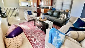 En moderne stue med en sofa, lænestole og et sofabord. Der er et køkkenområde med skabe og et spisebord.