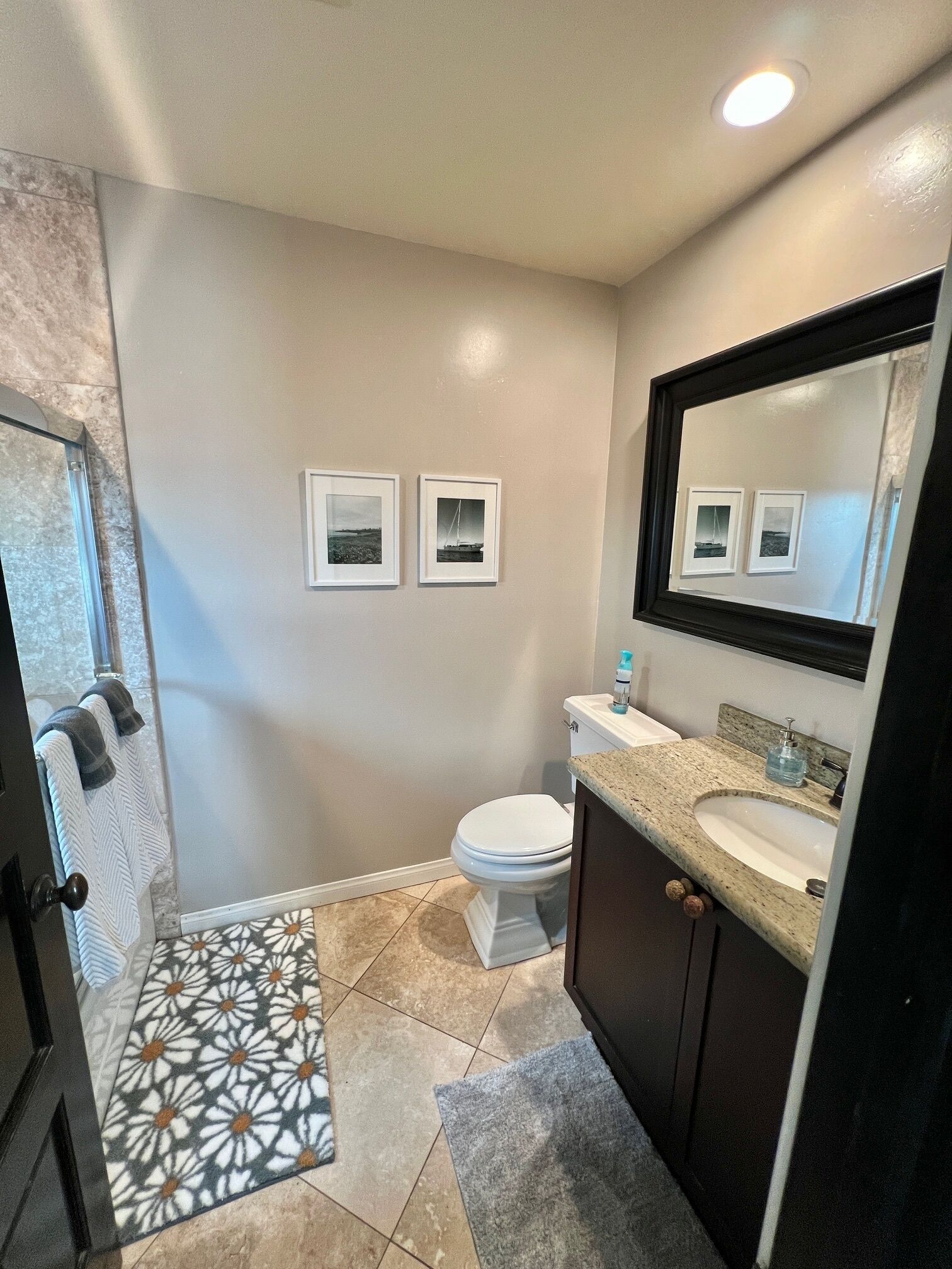A bathroom with a white toilet, a sink with a mirror above it, and two framed pictures on the wall.