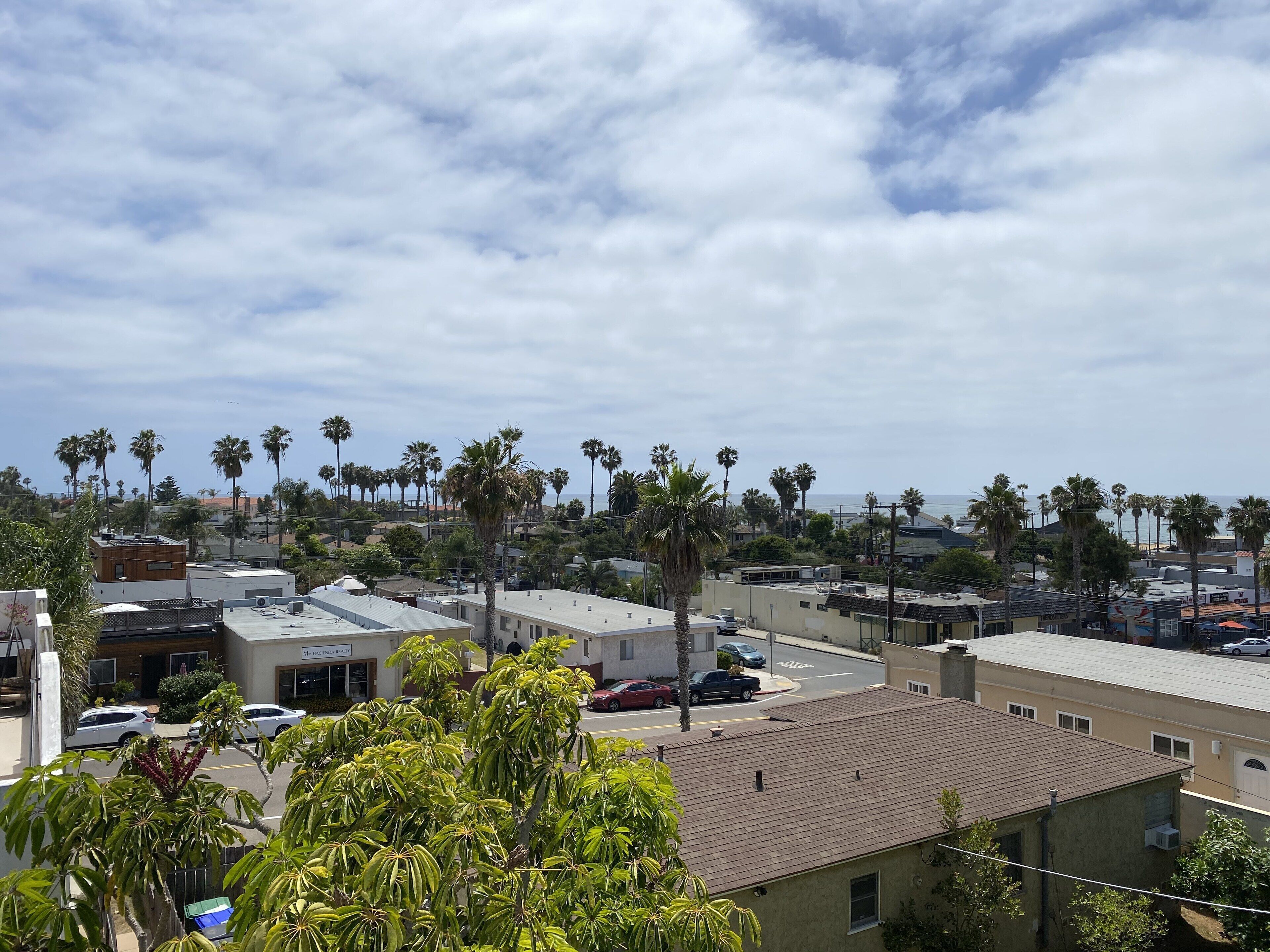 A residential area with multiple-story buildings, palm trees, and parked cars.