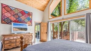 A bedroom with a large bed, a wooden dresser, a television, and a colorful tapestry. - Large, Beautiful Cabin on Tonto Creek in Kohl's Ranch /Game Room/Hot Tub/Views (Payson)