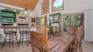 A spacious kitchen with wooden cabinets, a large dining table, and bar stools. - Large, Beautiful Cabin on Tonto Creek in Kohl's Ranch /Game Room/Hot Tub/Views (Payson)
