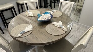 Ein runder Esstisch mit Tischsets, einer Schale Muscheln und gefalteten Servietten.