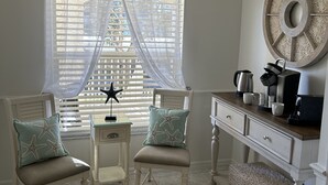Ein gemütliches Zimmer mit zwei weißen Stühlen, einem kleinen Tisch, einer Kaffeemaschine und einer dekorativen Felge an der Wand.