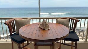 Une table en bois avec deux chaises, sur un balcon donnant sur l’océan.