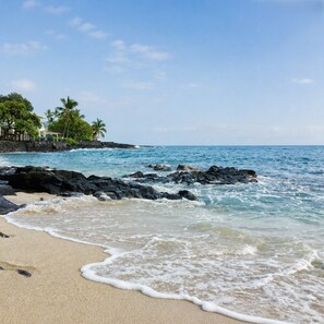 A beach with waves, a rocky shoreline, and a building with a view of the ocean.