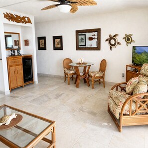A living room with a television, a dining table with chairs, a sofa, a glass coffee table, and a ceiling fan.