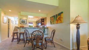 A dining area with a central island, surrounded by wooden chairs and a carpeted floor. - Condo in Kapalua!! (Maui)