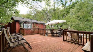 Una terraza de madera con mobiliario exterior, una parrilla de barbacoa y un espacio cubierto con sombrilla.