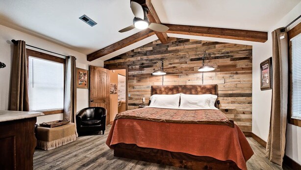 Un dormitorio con cabecera de madera, cama con colcha marrón, ventilador de techo y ventana con cortinas.