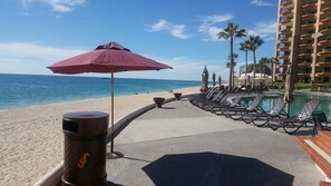 Un complexe hôtelier situé en bord de mer, doté d’une piscine, de chaises longues et de palmiers.