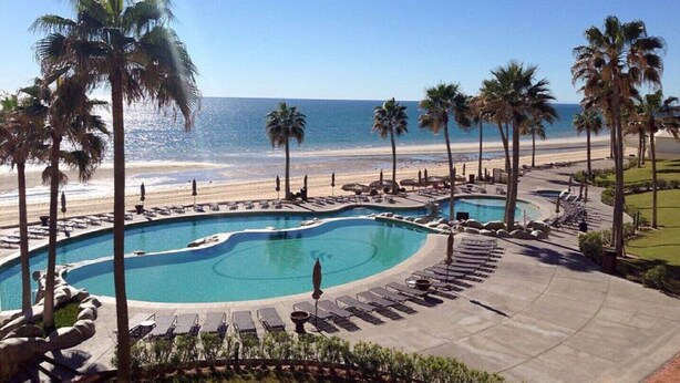 A pool area with multiple swimming pools, palm trees, and a beach view.