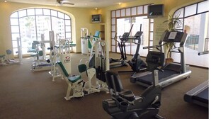 A gym with various exercise machines, large windows, and a ceiling fan.
