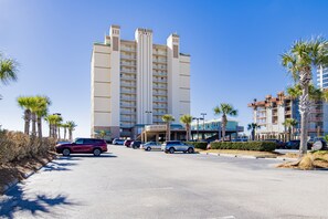 A multi-story hotel with a central entrance, parking lot, and palm trees.