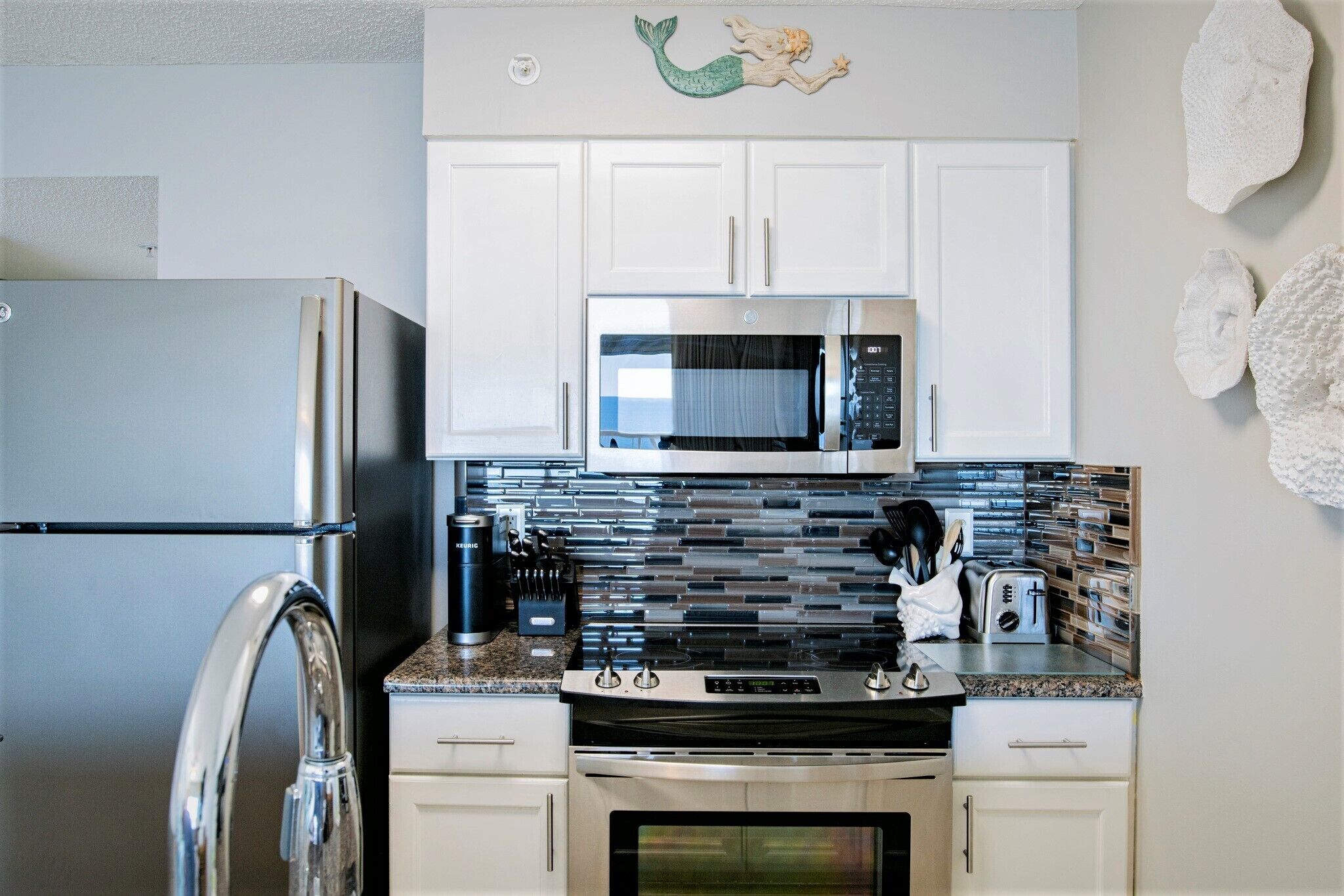 A modern kitchen with white cabinets, a stainless steel refrigerator, a microwave, and a granite countertop.