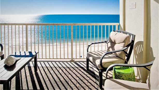 Ein Balkon mit Blick auf Strand und Meer, ein Stuhl, ein kleiner Tisch und eine grüne Vase.