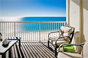 Un balcone con vista sulla spiaggia e sull'oceano, una sedia, un tavolino e un vaso verde.