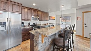 Une cuisine moderne dotée d’un grand îlot central, d’appareils électroménagers en acier inoxydable et d’un mur décoratif en pierre.