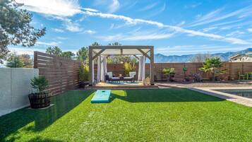 Enjoy a serene setting with a lush lawn, pergola, and seating area surrounded by potted plants and a wooden fence.