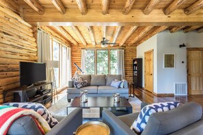 Interior de una cabaña de troncos con sala de estar, un sofá, una mesa de centro y un televisor.