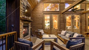 Interior acogedor de una cabaña con chimenea de piedra, muebles de madera y ventilador de techo.