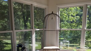 A sunlit room with large windows, a birdcage, a small table with a lantern, and a blue rug.