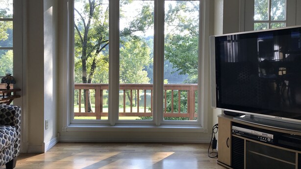 A room with a large window, a flat-screen TV, and a wooden deck outside.