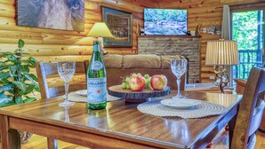A wooden interior with a dining table set for two, a bottle of Pellegrino water, a fruit platter, and a television mounted on the wall. - FREE Dollywood and Attractions daily with stay MTN View Cabin Pool Table Hot tub (Gatlinburg)