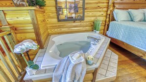 A wooden cabin interior with a wooden bed, a bathtub, a small potted plant, and a window with a reflection. - FREE Dollywood and Attractions daily with stay MTN View Cabin Pool Table Hot tub (Gatlinburg)