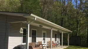 A single-story cabin with a porch, outdoor seating, and a trash can. - Great Fishing! Quiet & Relaxing!  Close to Casino & Mingo Falls! (Cherokee)
