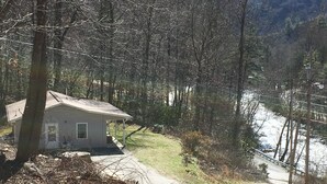 A small house with a porch, surrounded by trees and a river. - Great Fishing! Quiet & Relaxing!  Close to Casino & Mingo Falls! (Cherokee)