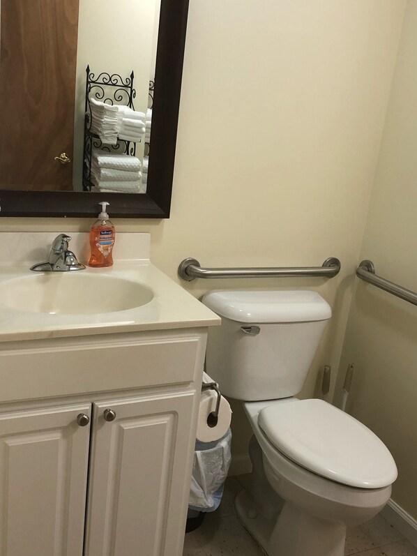 Un baño con un lavamanos blanco, un espejo, un inodoro y un pasamanos.