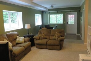 A living room with two sofas, a coffee table, and a lamp. There are two windows providing natural light.