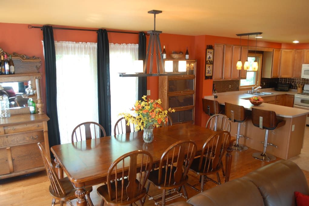 Een eetgedeelte met een houten tafel en stoelen, een vaas met bloemen, en een keuken met houten kastjes en een bar.