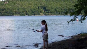 Una persona pescando en un lago con una colina boscosa al fondo.