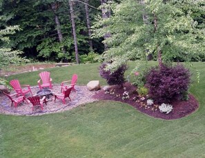 A patio with red chairs and a table, surrounded by a landscaped garden with various shrubs and a tree.