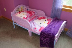 A small child's bed with a Hello Kitty-themed bedspread and a purple blanket.