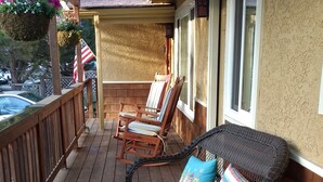 Une terrasse en bois avec des meubles en osier, notamment une chaise et une petite table, ainsi qu’un pot à fleurs suspendu.